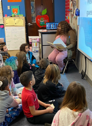 Ms. Daysha reads a story to children that are seated around her on the floor. 