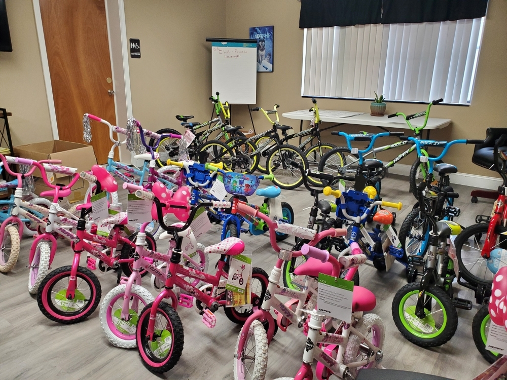Twenty five bicycles lined up in a room. The bikes vary in size and colors for young children. 
