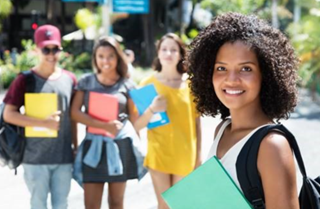 Young man holding a book with her fellow classmates standing behind her. 