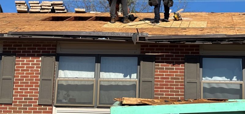 Two men standing on the roof of a housing unit, working with shingles. 